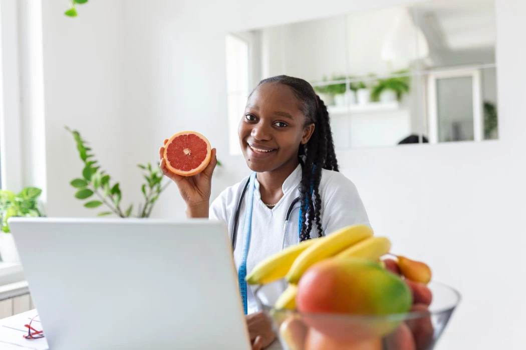Portrait of young smiling female nutritionist in the consultation room Nutritionist desk with healthy fruit juice and measuring tape Dietitian working on diet plan