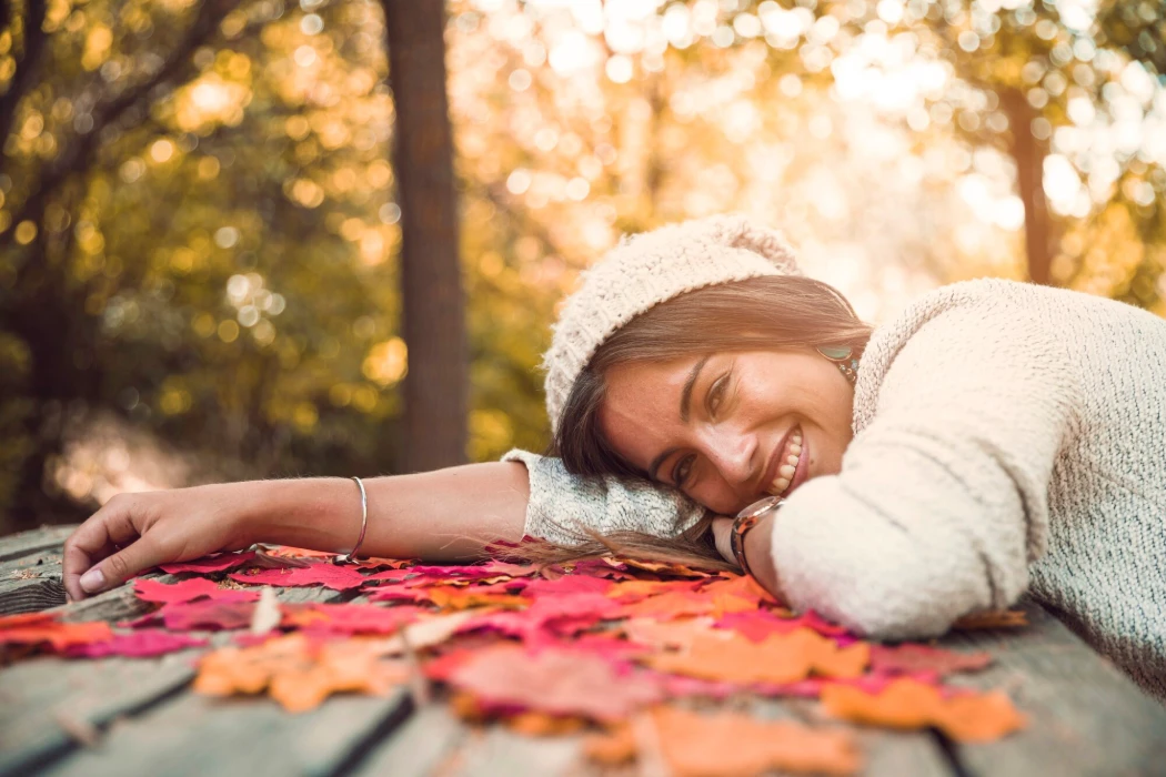 Cheerful woman lying on table with autumn leaves