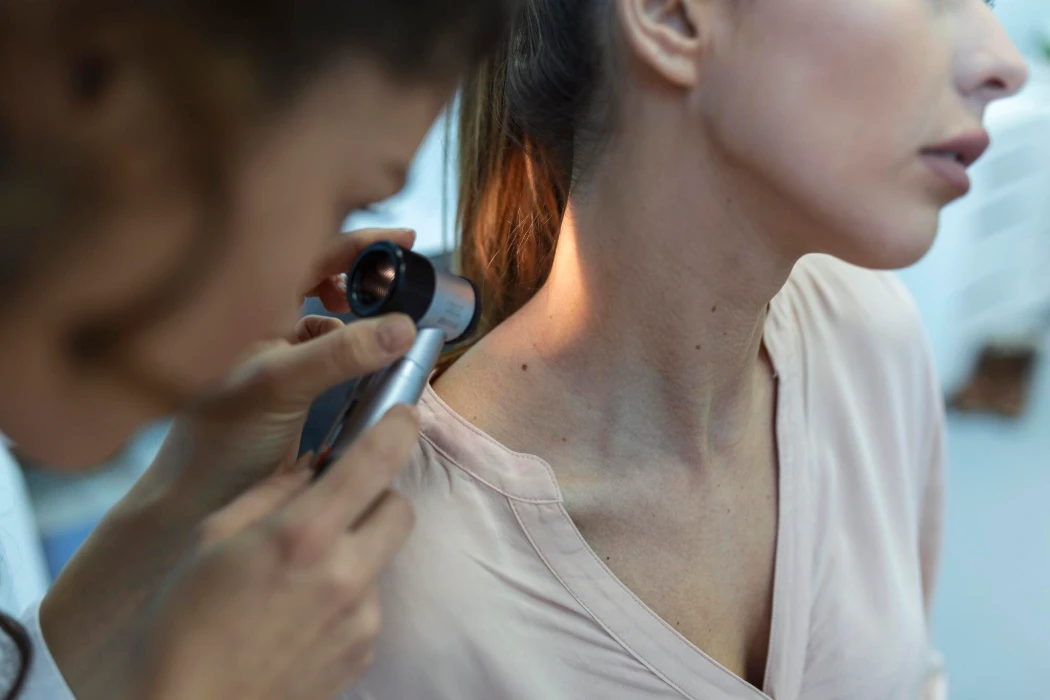 Dermatologist in latex gloves holding dermatoscope while examining attractive patient with skin disease Female dermatologist examining patient with dermascope looking for signs of skin cancer